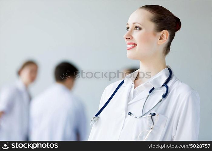Young female doctor. Attractive female doctor in white uniform with colleagues at background