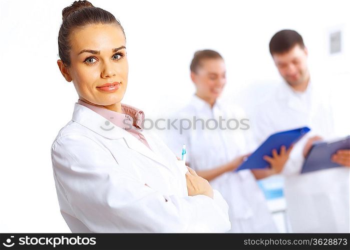 Young female doctor in white uniform with collegues on the background