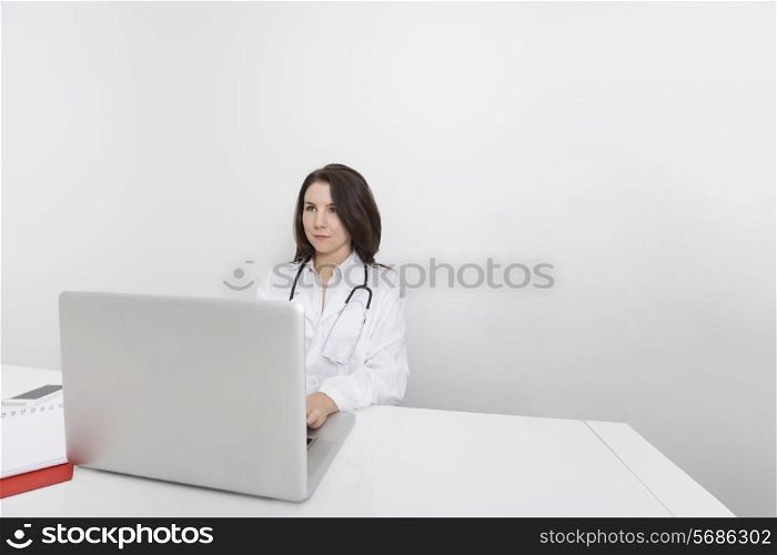 Young female doctor looking away while using laptop at desk in clinic