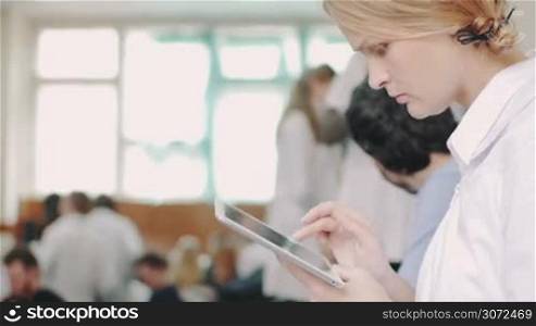 Young female doctor or medical student typing on digital tablet during the break on lecture or conference