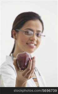Young female doctor recommending an apple isolated over white background