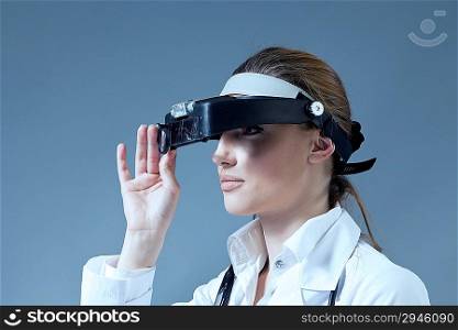 Young female doctor wearing magnifying glass equipment on her had. Medical / pharmaceutical research concept. Healthcare collection.