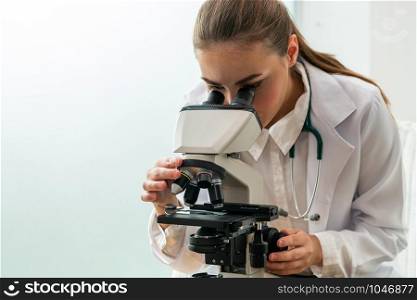 Young female doctor working using microscope in hospital laboratory. Medical and medicine technology research and development concept.