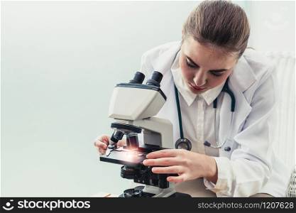 Young female doctor working using microscope in hospital laboratory. Medical and medicine technology research and development concept.