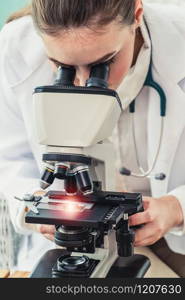 Young female doctor working using microscope in hospital laboratory. Medical and medicine technology research and development concept.