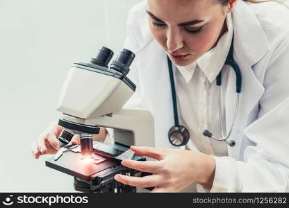 Young female doctor working using microscope in hospital laboratory. Medical and medicine technology research and development concept.