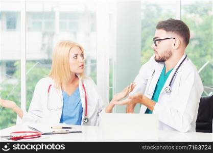 Young female doctor works at office in hospital while talking to male doctor sitting beside her. Medical service and healthcare concept.
