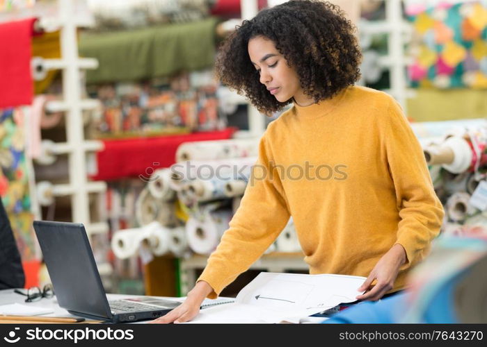 young female dressmaker choosing material from catalogue in studio