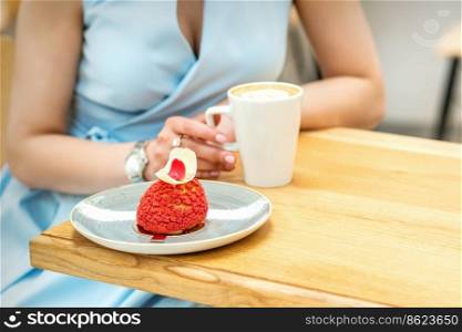 Young female drinking coffee with a piece of cake sitting at the table in a cafe outdoors. Young female drinking coffee in cafe
