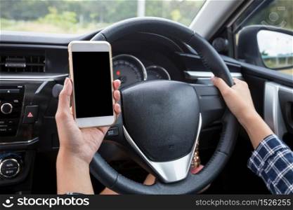 Young female driver using touch screen smartphone and hand holding steering wheel in a car.