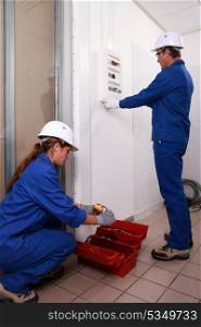 young female electrician and mature instructor looking at electric meter