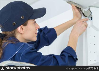 young female electrician installing electrical socket on wall with screwdriver