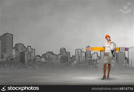 Young female engineer in hard hat with big pencil. Woman architect