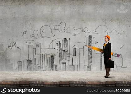 Young female engineer in hard hat with big pencil. Woman architect