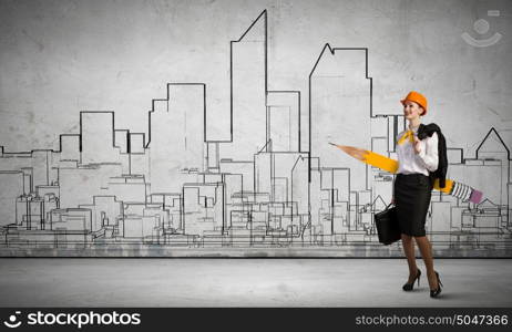 Young female engineer in hard hat with big pencil. Woman architect