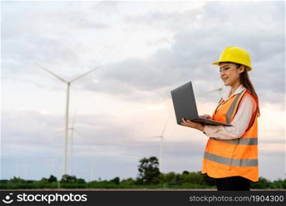 young female engineer working with laptop computer against wind turbine farm