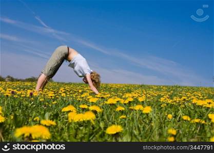young female excercising yoga on flowery meadow