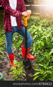 Young female farmer posing with shovel on garden bed at sunny day