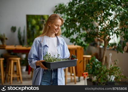 Young female florist worker enjoying her job. Portrait of smiling woman walking with plants in plastic box. Floristic workshop concept. Young female florist worker enjoying her job