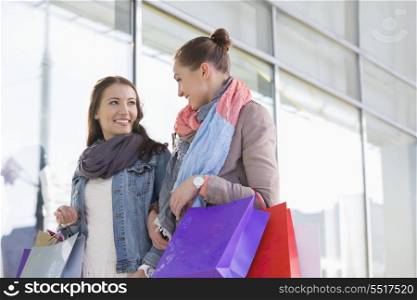 Young female friends looking at each other against store
