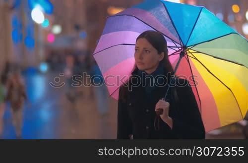 Young female friends meeting in the street, giving each other friendly kisses and hugs and walking away under colorful umbrella to spend a nice evening together