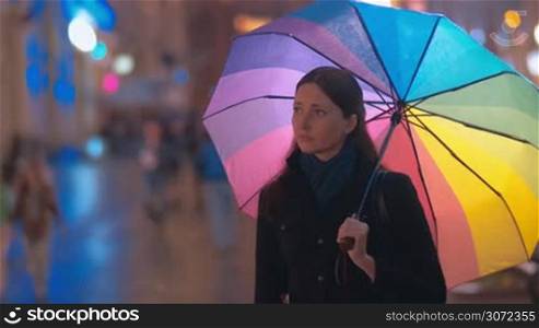 Young female friends meeting in the street, giving each other friendly kisses and hugs and walking away under colorful umbrella to spend a nice evening together