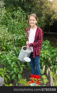 Young female gardener watering garden bed with ripe vegetables