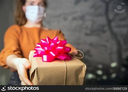 Young Female holding a kraft paper gift box with pink decoration with medical protective face mask for Coronavirus, Covid-19 and present concept. Birthday or Valentines day retro design romantic. Young Female holding a kraft paper gift box with pink decoration with medical protective face mask for Coronavirus, Covid-19 and present concept. Birthday or Valentines day retro design