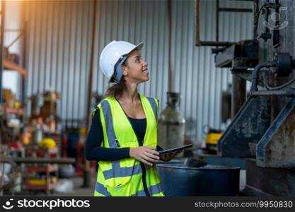 Young female in protective uniform inspecting industrial machine and taking necessary notes on digital tablet at plant.