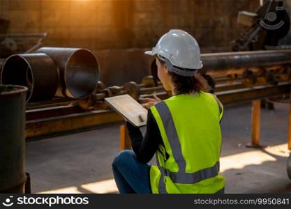 Young female in protective uniform inspecting industrial machine and taking necessary notes on digital tablet at plant.