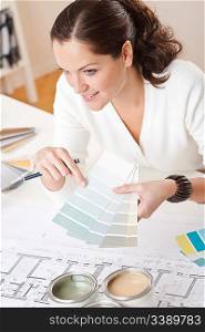 Young female interior designer working at office with color swatch and can of paint