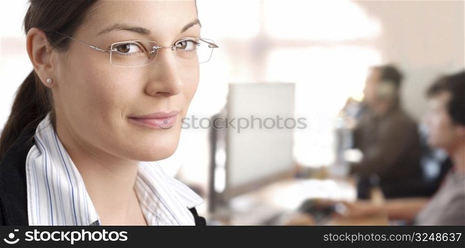 Young female manager stands in the office with IT specialists are working in the background.
