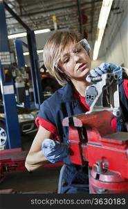 Young female mechanic in protective workwear working on machinery part in automobile repair shop