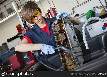 Young female mechanic working with welding torch on vehicle machinery part in auto repair shop