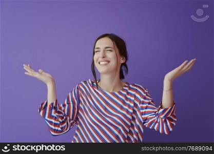 Young female model with open wide arms posing over purple and yellow background. Girl in modern fashionable clothes standingl in the studio with stretched hands. Surprised expression