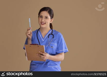 Young female nurse in blue scrubs with a stethoscope around her neck, holding a clipboard and pen