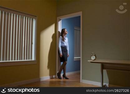 Young female office worker leaning against door frame and with alarm clock in the foreground