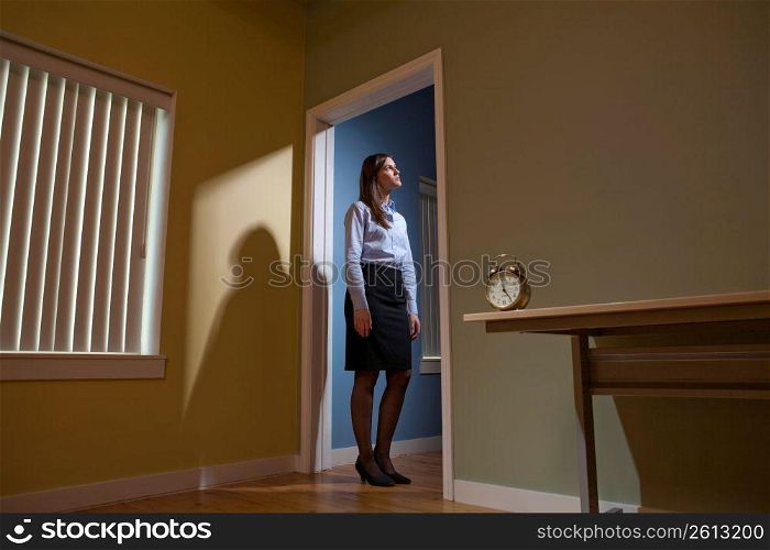 Young female office worker standing in a doorway, alarm clock in the foreground