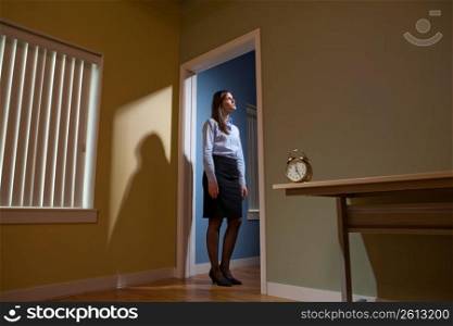 Young female office worker standing in a doorway, alarm clock in the foreground