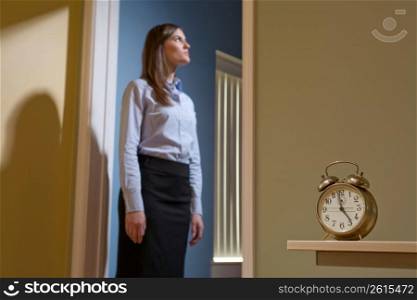 Young female office worker standing in a doorway, focus on the alarm clock in the foreground