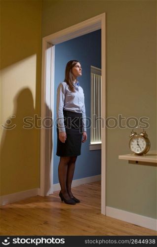 Young female office worker standing in a doorway, focus on the alarm clock in the foreground