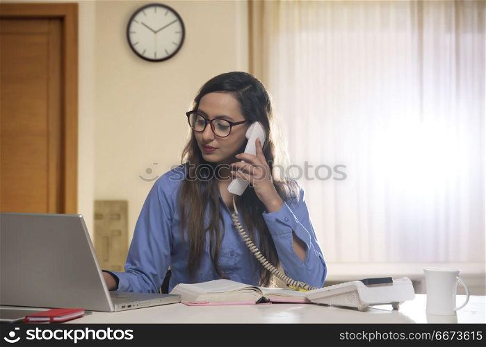 Young female office worker using telephone and laptop computer