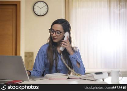 Young female office worker using telephone and laptop computer