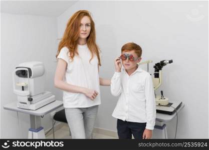 young female optician looking camera while examine boy patient eyes