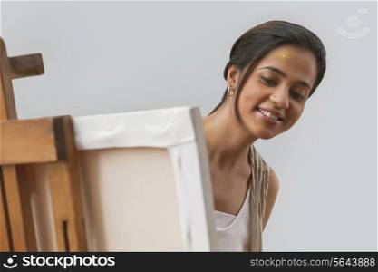 Young female painter looking at painting over gray background