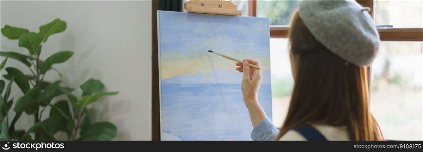 Young female painter using paintbrush to drawing and painting masterpiece on canvas in home studio.
