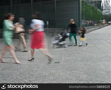 young female parent with stroller rushing on the street in intentional motion blur, business people walking by