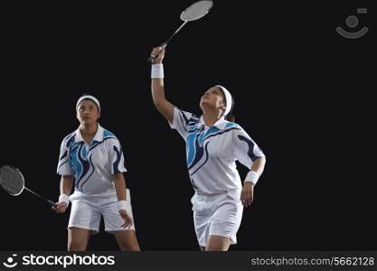 Young female partners in sportswear playing badminton against black background
