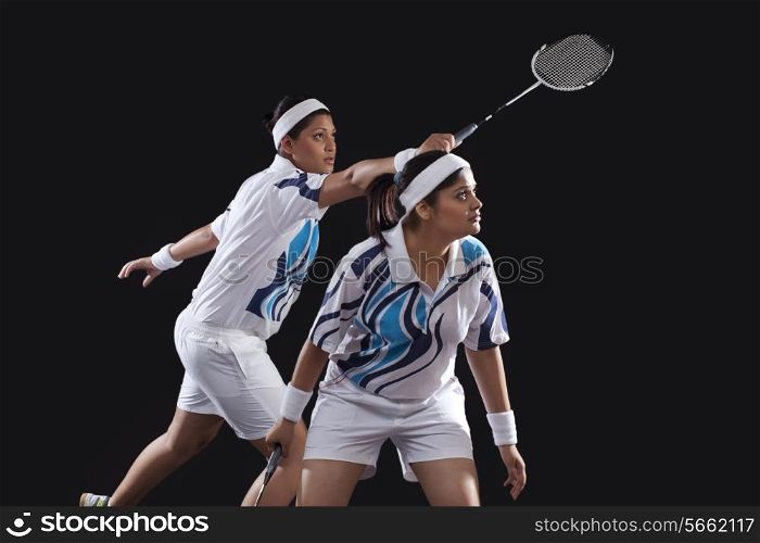 Young female partners in sportswear playing badminton over black background