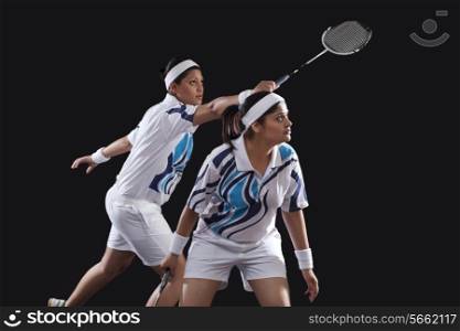 Young female partners in sportswear playing badminton over black background
